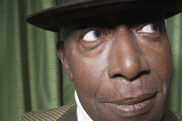 Closeup of an African American senior man wearing a hat against green curtain