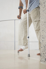 Low section of man with broken leg walking with crutches at home