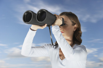 Businessman looking through large binoculars against blue sky