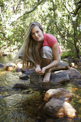 Portrait of teenage girl squatting on stone by forest stream