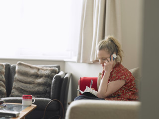 Young woman with diary using mobile phone in living room