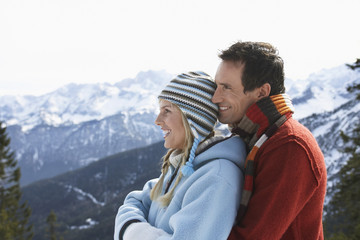 Side view of a happy loving couple in warm clothing against snow covered mountain
