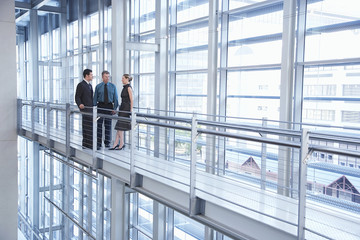 Full length of business people discussing by railing in modern office