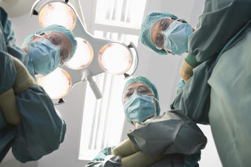 Low angle view of three confident surgeons under lights in operating theatre