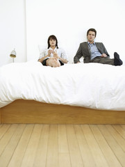 Young business couple sitting on bed, ignoring