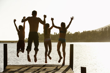 Rear view of father with children holding hands while jumping off a jetty