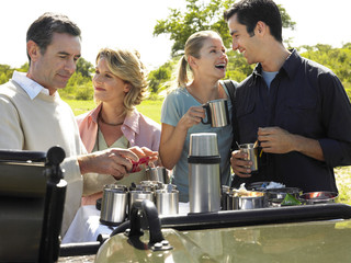 Two happy couples having picnic with trees in background