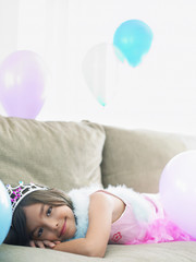 Portrait of a young smiling girl lying on sofa with balloons