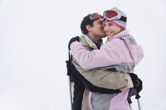 Side view of a happy couple in warm clothing embracing in snow