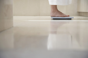 Low section of woman standing on weighing scale in bathroom