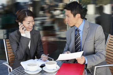 Businesspeople reviewing documents at an outdoor cafe while on call