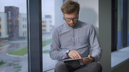 Young businessman is sitting at window and browsing