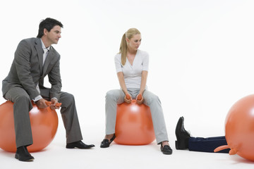 Young couple sitting on space hoppers and looking at fallen man against white background