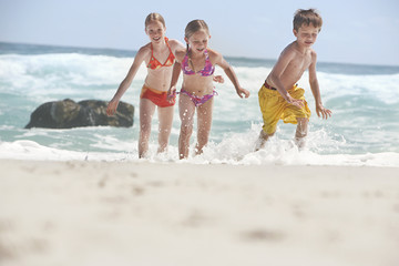 Cheerful little siblings running in water at beach