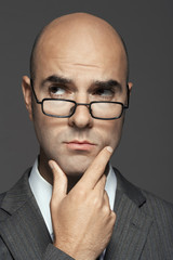 Closeup of a bald businessman wearing glasses with hand on chin against gray background