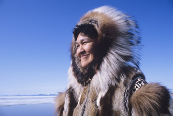 Smiling Eskimo woman wearing traditional clothing in wind against clear blue sky - obrazy, fototapety, plakaty