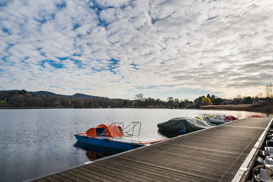 Panorama of Lake Monate with a sky with stratocumulus, in the foreground a wooden floating dock with pedal boats