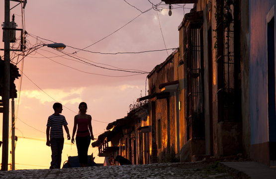 Two young people in silhouette at sunset on cobbled street with colourful orange sky behind, Trinidad, Cuba 