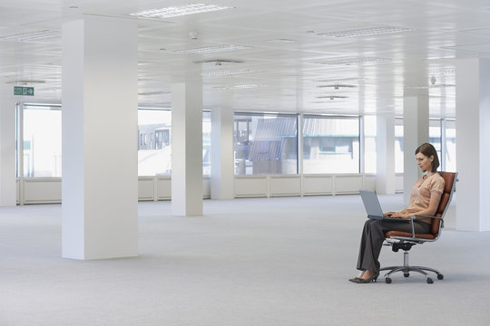 Full Length Of Young Businesswoman Using Laptop On Chair In Empty Office Space