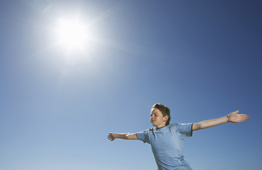 Young boy with arms outstretched in front of blue sky