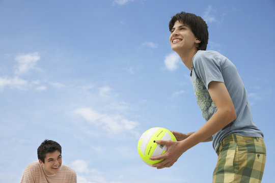 Low Angle View Of Happy Teenage Boys Playing Beach Volleyball Against Sky