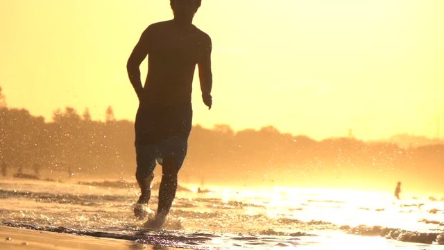SLOW MOTION: Young sportsman running in shallow water on beautiful sunset beach