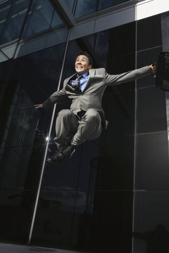 Low angle view of a young businessman with briefcase jumping outside office building