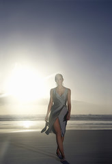 Full length of young woman in evening dress walking on beach