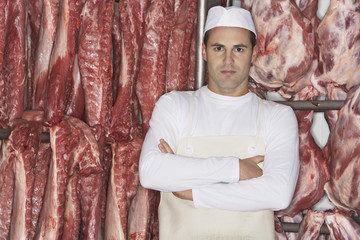 Portrait of a butcher standing with arms crossed in front of raw meat 