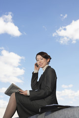 Low angle view of a young businesswoman using cellphone with newspaper against sky