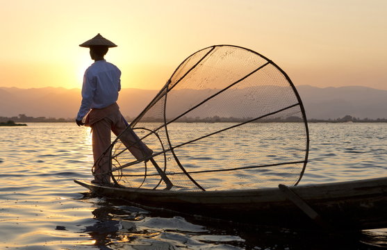 Intha 'leg rowing' fishermen at sunset on Inle Lake who row traditional wooden boats using their leg and fish using nets stretched over conical bamboo frames, Inle Lake