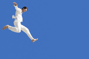 Fototapeta na wymiar Full length of young businessman jumping against blue sky