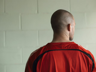 Rear view of a bald soccer player against green wall