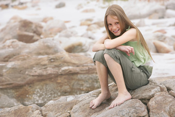 Portrait of happy little girl sitting on rock at beach