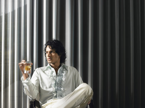 Young Indian man sitting with an alcoholic drink in front of curtain