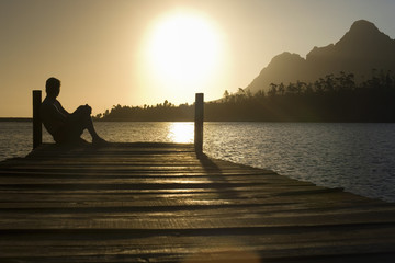 Side view of man sitting on dock by lake enjoying sunset