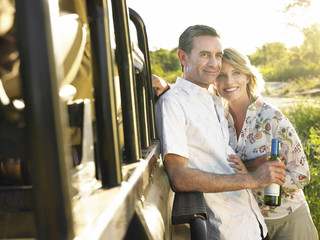 Smiling adult couple standing by jeep with a bottle of wine