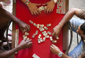 Overhead view of four people playing dominos on a red table using dominos marked with Cuba and the Cuban flag, Havana, Cuba