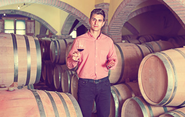 Male customer tasting red wine from wooden barrels