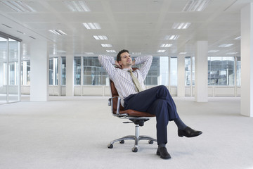 Full length of relaxing young businessman on chair in empty office space