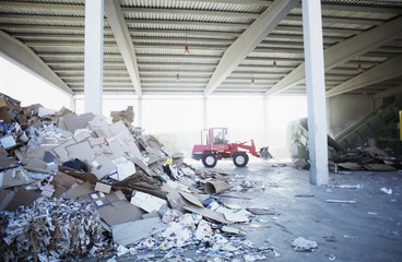 Heap of paper waste with digger truck in background at recycling plant