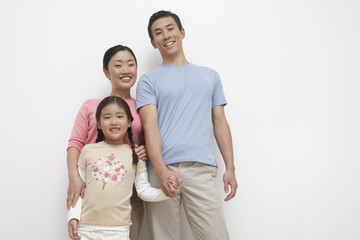Fototapeta premium Portrait of a young couple with daughter standing against white background