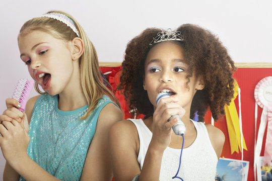 Multiethnic young girls using brushes as microphones to sing at a slumber party