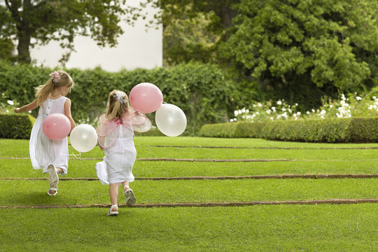 Rear view of little bridesmaids with balloons running in garden
