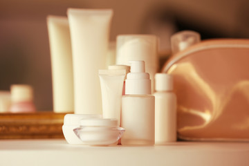 Bottles and jars with cream on white table against blurred background, close up view