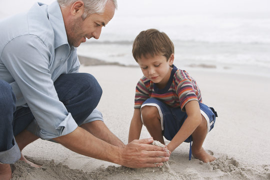 Closeup of father and son making sand castle together on beach