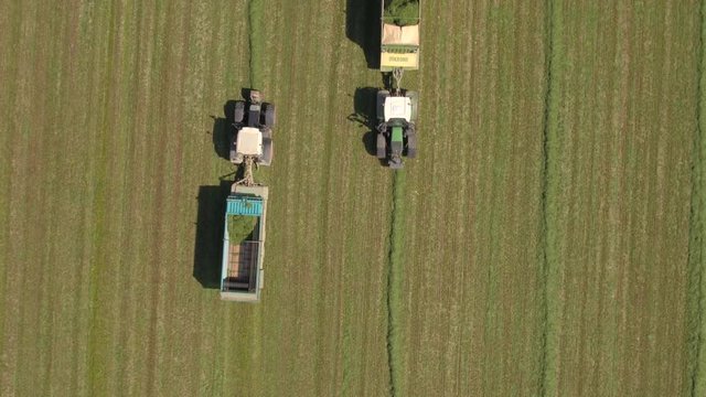 Aerial farmers in tractors working on farm field collecting hay fodder in wagon