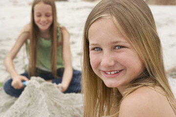 Portrait of cute little girl smiling with sister making sand castle in background at beach