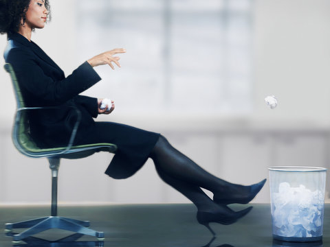 Businesswoman On Chair Throwing Paper Ball Into Dustbin