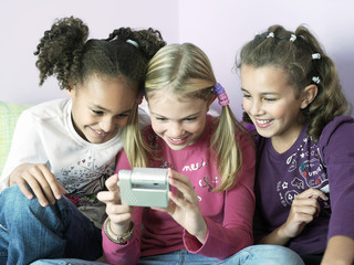 Young girls sitting side by side and playing with electrical gadget